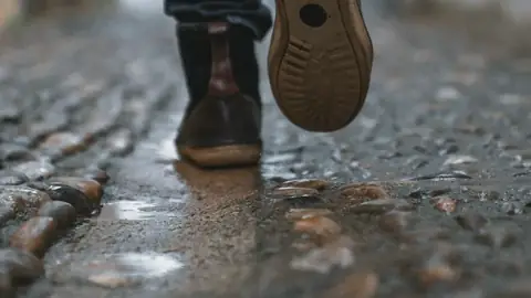Unos pies caminando por una calle mojada