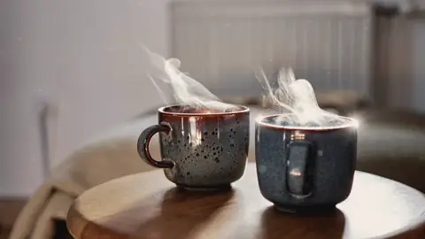 Dos tazas humeantes sobre una mesa redonda de madera