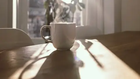 Una taza humeante en una mesa junto a la ventana